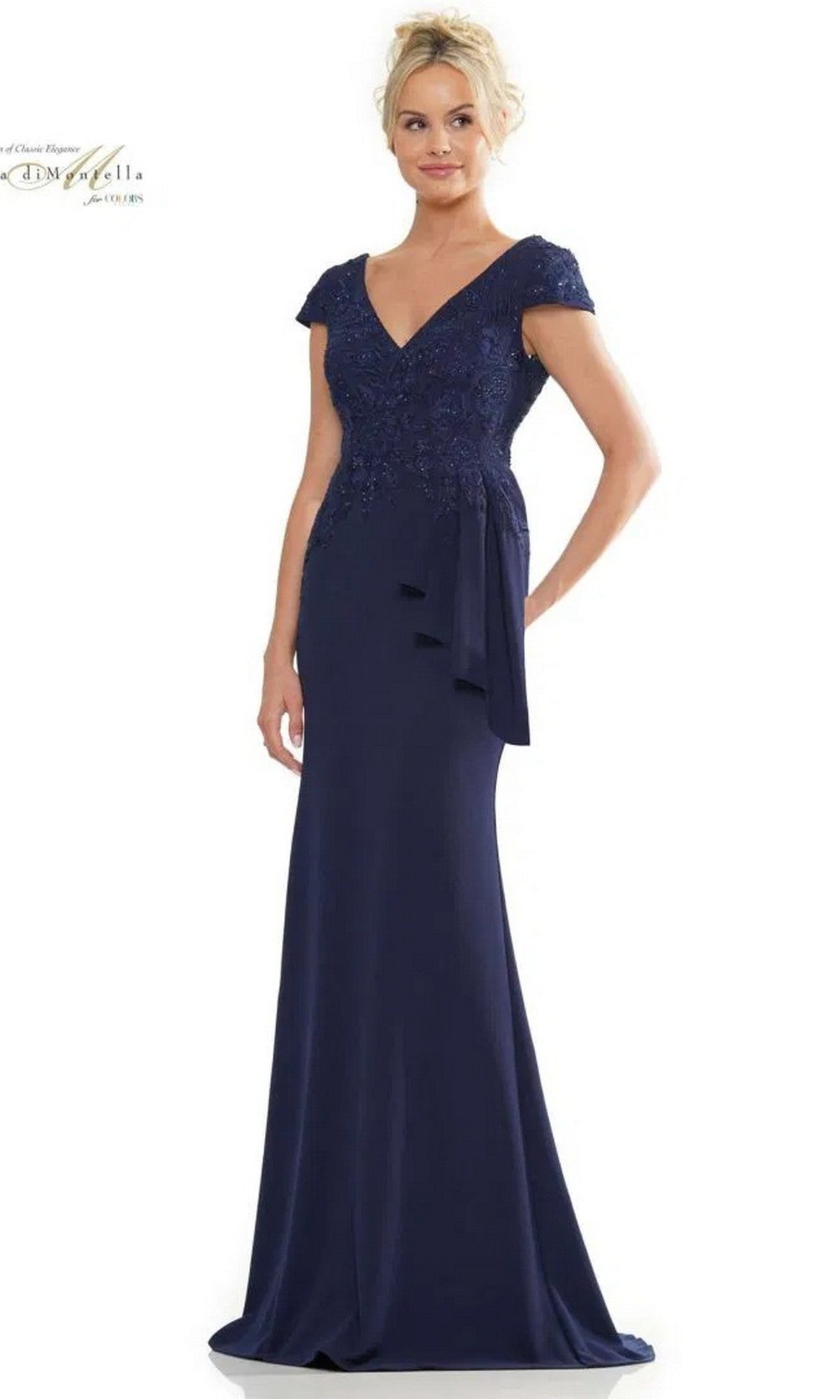 A woman stands against a white background wearing the Rina Di Montella RD2960 Long Formal Dress in navy, featuring a floor-length stretch crepe design with short sleeves, V-neckline, embroidered bodice, and draped side detail.